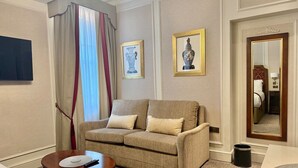 A hotel room with a sofa, a small table, a mirror, and framed artwork on the wall.