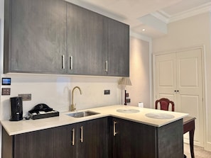A kitchen with dark cabinets, a countertop, a sink, and a coffee maker. - New Studio Flat with AC, Marylebone (Greater London)