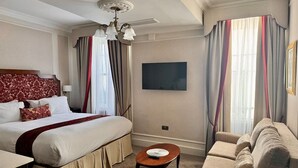 A hotel room with a bed, a sofa, a TV, and a chandelier.