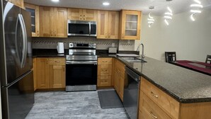 A modern kitchen with wooden cabinets, stainless steel appliances, and a marble floor.