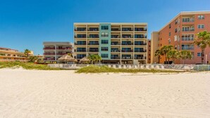A beachfront hotel with multiple floors, balconies, and a sandy beach in the foreground.