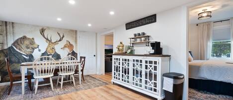 A dining area with a wooden table and chairs, a white cabinet with glass doors, and a mural of deer on the wall.