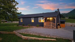 A dark-colored house with a wooden porch and a gravel driveway.