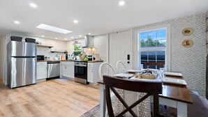 A modern kitchen with stainless steel appliances, white cabinetry, and a dining area with a wooden table and chairs.