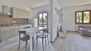 A modern kitchen with white cabinets, a dining area with a white table and four chairs, a TV on a stand, and a sofa with a patterned cover. - Bilocale Ida - Goelba (Campo nell'Elba)