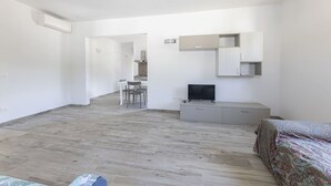 A modern, minimalistic room with a wooden floor, a bed, a TV, a desk, and a chair. - Bilocale Ida - Goelba (Campo nell'Elba)
