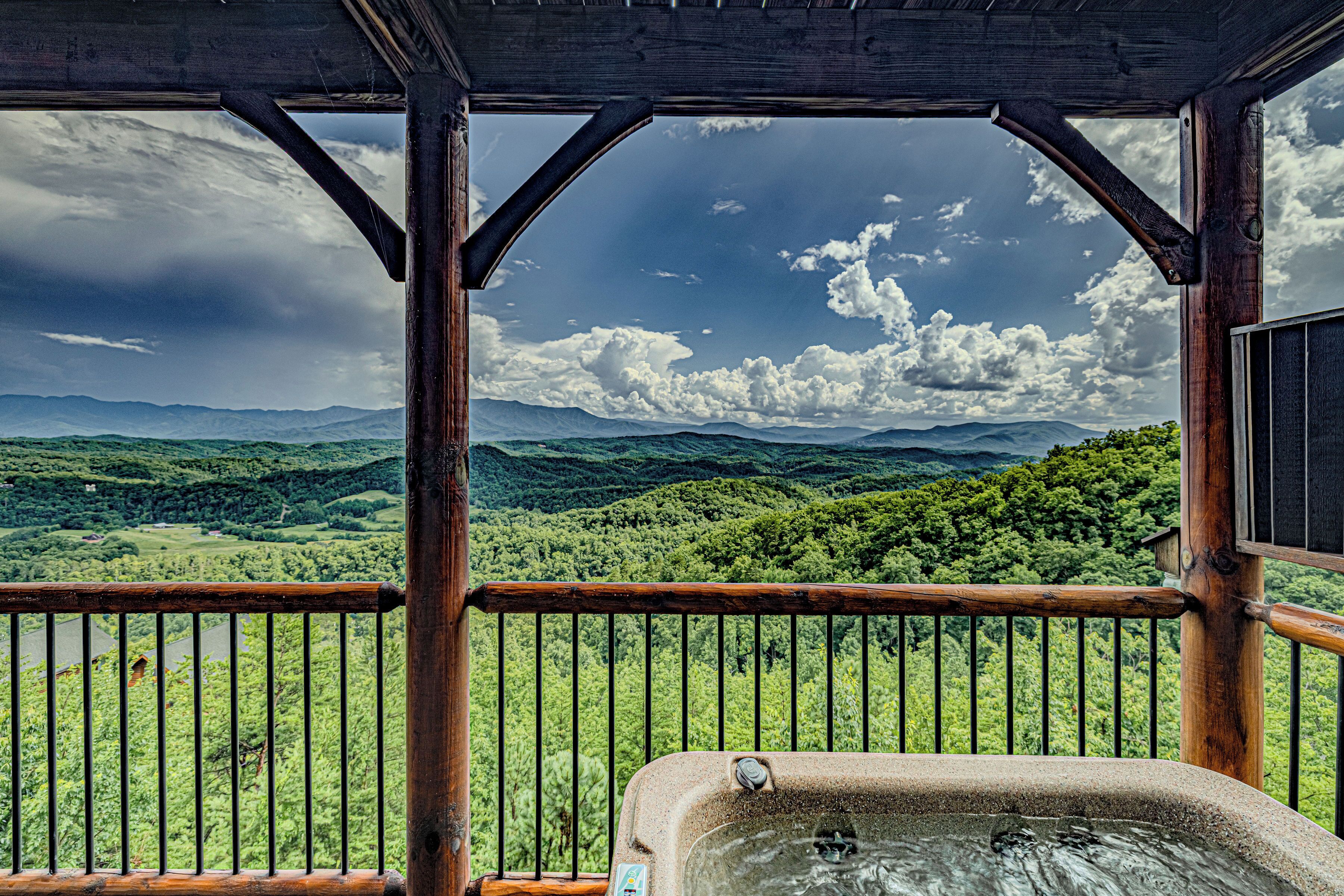 A wooden balcony with a hot tub, overlooking a lush green landscape and mountains.