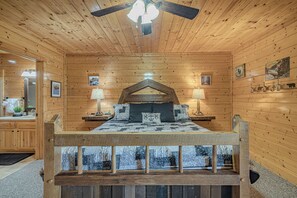 A wooden cabin bedroom with a bed, a ceiling fan, and a view of a snowy landscape through the window. - Unobstructed Views, Hot Tub, Game Room, Arcade, Family Retreat (Sevierville)