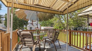 A covered outdoor deck with wooden railings, a glass table, and two chairs.