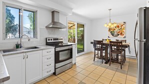 A modern kitchen with white cabinets, a stainless steel range, and a dining area with a table and chairs.
