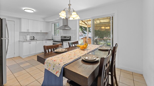A modern kitchen with white cabinets, a dining table with a floral tablecloth, and a view of the outdoors through large windows.