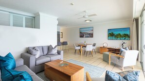 A modern living room with a grey sofa, a wooden coffee table, and a dining area with a table and chairs. - Beach Front Hamilton Island (Whitsundays)