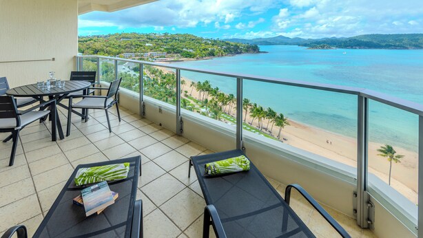 A balcony with a table and chairs, overlooking a beach and turquoise sea. - Beach Front Hamilton Island (Whitsundays)