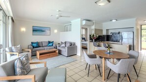 A modern living room with a grey sofa set, a wooden coffee table, and a dining area with a wooden table and grey chairs. - Beach Front Hamilton Island (Whitsundays)