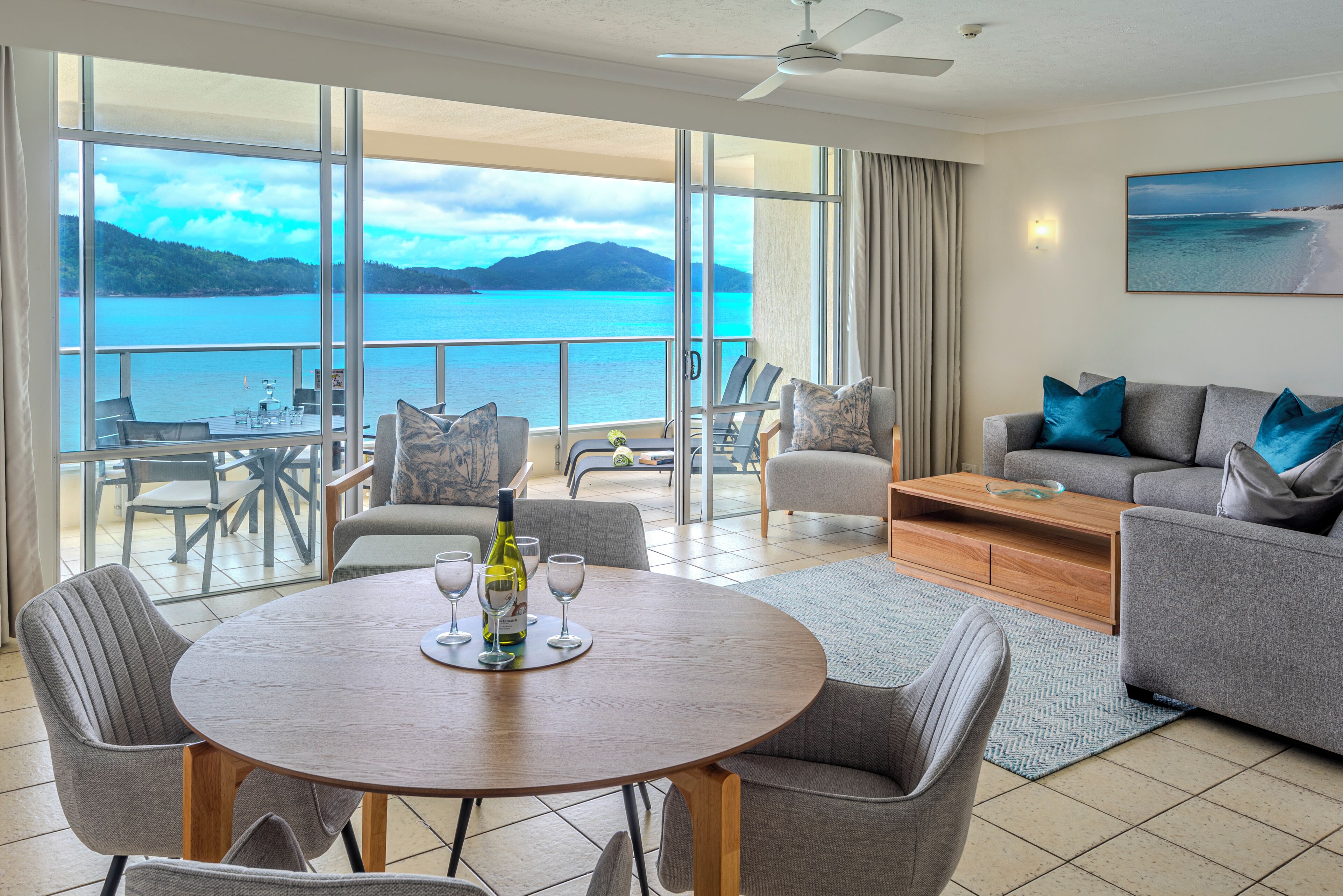A spacious living area with a balcony overlooking a body of water and mountains.