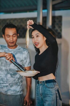 Two people in a room with a table, one holding a fish and the other holding a plate. - VILLA GIO BIEN LAGI (Phuoc Hoi)