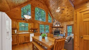 L’intérieur d’une cabane avec des murs en bois, de grandes fenêtres, une table à manger et une cheminée.