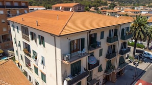 Un immeuble à plusieurs étages doté de balcons, d’un toit en tuiles et offrant une vue sur une rue et des collines en arrière-plan.