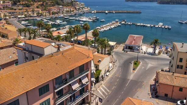 Une ville côtière dotée d’un port de plaisance, de bâtiments aux toits recouverts de tuiles rouges et offrant une vue dégagée sur la mer.