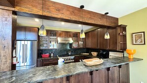 Une cuisine dotée de meubles en bois, d’un réfrigérateur en acier inoxydable, d’un plan de travail en granit et de luminaires suspendus.