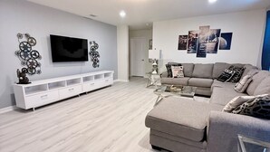 A modern living room with a grey sofa, a white entertainment unit, and a flat-screen TV.