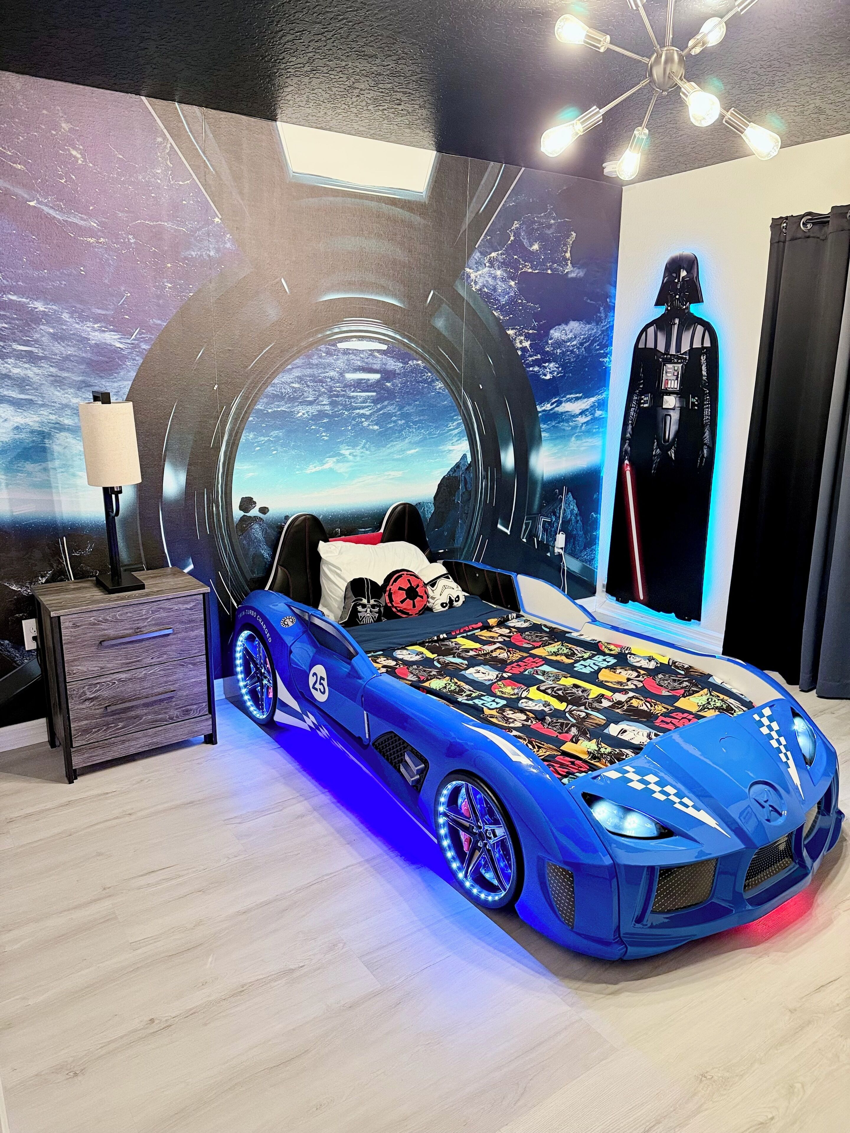 A bedroom with a bed featuring a space-themed mural, a blue sports car design, and a Darth Vader poster.
