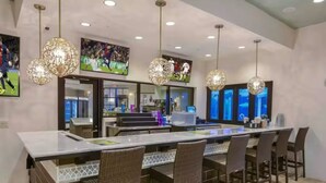 A modern bar area with a long counter, wicker chairs, and decorative hanging lights.