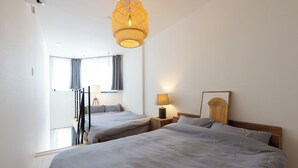 A hotel room with two beds, a window with curtains, a hanging light fixture, and a bedside table with a lamp. - Less than 10 minutes from each of Shibuya, Shinjuku and Harajuku/ Central location/ New construction/ Max. 6 people (渋谷区)