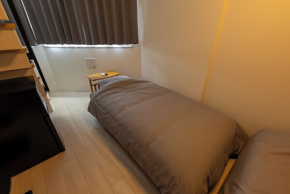 A small, single-bed room with a wooden floor, a desk, and a window with blinds. - Less than 10 minutes from each of Shibuya, Shinjuku and Harajuku/ Central location/ New construction/ Max. 6 people (渋谷区)