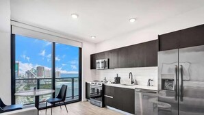 A modern kitchen with a large window, a dining area with chairs, and a view of a cityscape.
