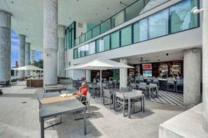 Un espace de restauration extérieur moderne, doté de tables et de parasols, d’un bar avec vue panoramique et d’un plafond haut avec des poutres apparentes.