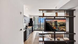 Un salon moderne doté d’un grand téléviseur à écran plat, d’un meuble de rangement épuré et offrant une vue sur le paysage urbain grâce à de grandes fenêtres.