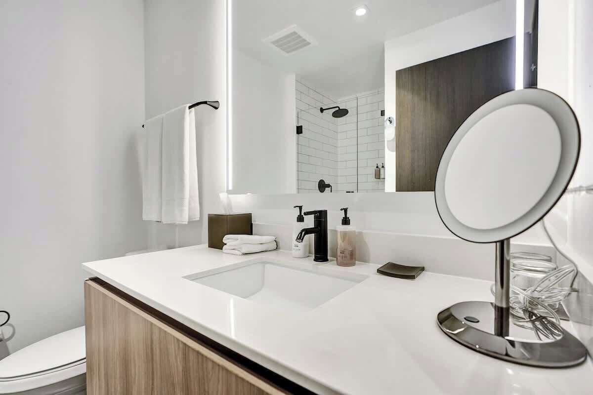 A modern bathroom with a white sink, a large mirror, and a towel rack.