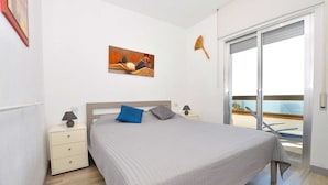 Une chambre à coucher comprenant un lit, une table de chevet, une lampe, un tableau au mur et une porte-fenêtre coulissante donnant sur un balcon.