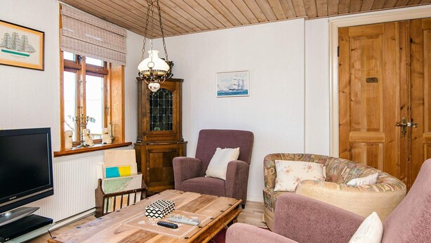 Ett mysigt vardagsrum med ett träpanelat tak, en tv, ett träbord och två soffor.