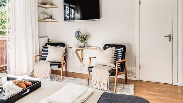 Een moderne slaapkamer met een bed, twee fauteuils, een televisie en een tafeltje met een plant.