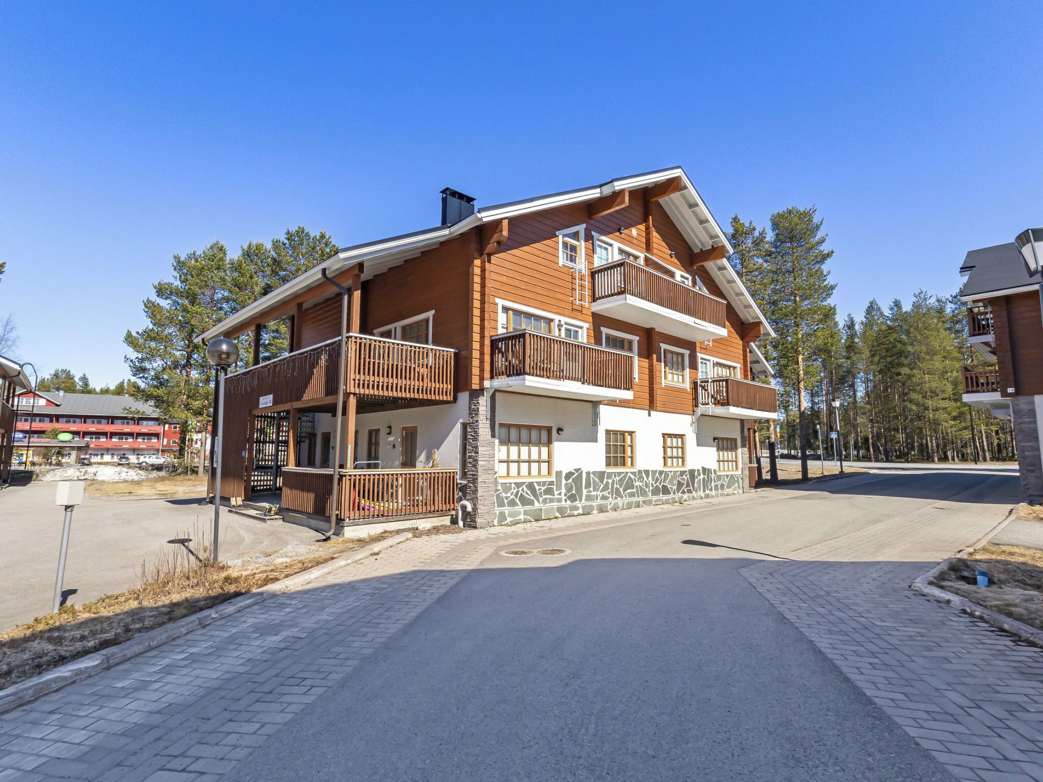 A multi-story building with balconies, a stone foundation, and a paved entrance area.