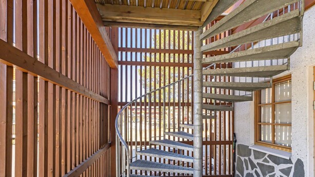 A spiral staircase with metal railings, wooden paneling on the walls, and a stone wall adjacent to a window. - Levin alppi 3 b 7 by Interhome (Kittilä)