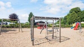 A playground with swings, a slide, and a small red building. - 2 Person Holiday Park Home in Aabenraa (Aabenraa)