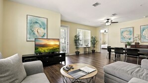 Un salon comprenant un téléviseur, un canapé, une table basse et un coin repas avec des chaises et une table.