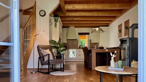 A spacious living area with a wooden staircase, a dining table, and a kitchen in the background.