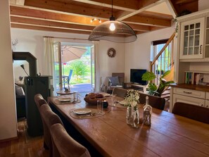 A dining area with a wooden table set for two, a grill, and a television in the background. - Lovely chalet with a garden near the ski slope (Kötschach-Mauthen)
