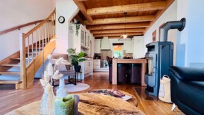 A spacious living area with a wooden staircase, a dining area, and a kitchen with a wood-burning stove.