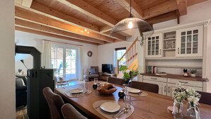 A dining area with a wooden table set for four, a chandelier, and a kitchen in the background.