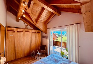 A bedroom with wooden ceiling beams, a bed, a chair, a small table, and a wardrobe. - Lovely chalet with a garden near the ski slope (Kötschach-Mauthen)
