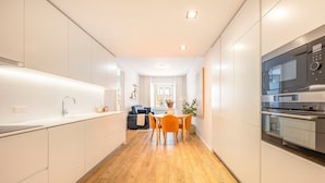Una cocina moderna con horno integrado, un comedor con mesa y sillas, y un pasillo que conduce a una sala de estar.