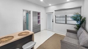 A modern living room with a grey sofa, a wooden coffee table with two decorative items, a small bar area with stools, and a bookshelf. - Condado Studio w/Pool  • Walk to Beach & Dining (San Juan)