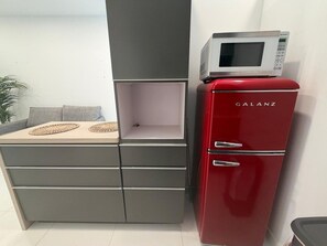 Une petite cuisine équipée avec un réfrigérateur rouge, un four à micro-ondes et un meuble gris doté de tiroirs.