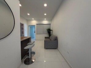 A modern kitchen with a bar area, a grey sofa, and a potted plant.