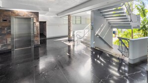 A spacious lobby with a polished black floor, a modern elevator, and a staircase leading to an outdoor area with greenery. - Condado Studio w/Pool  • Walk to Beach & Dining (San Juan)
